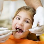 A dentist examining a child's teeth Description automatically generated with medium confidence